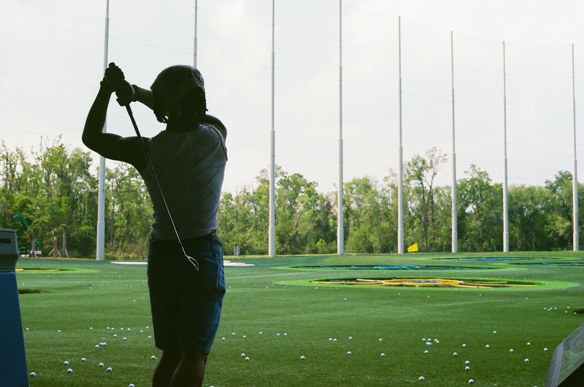 A golfer practicing at a driving range at dusk, balls scattered across the turf